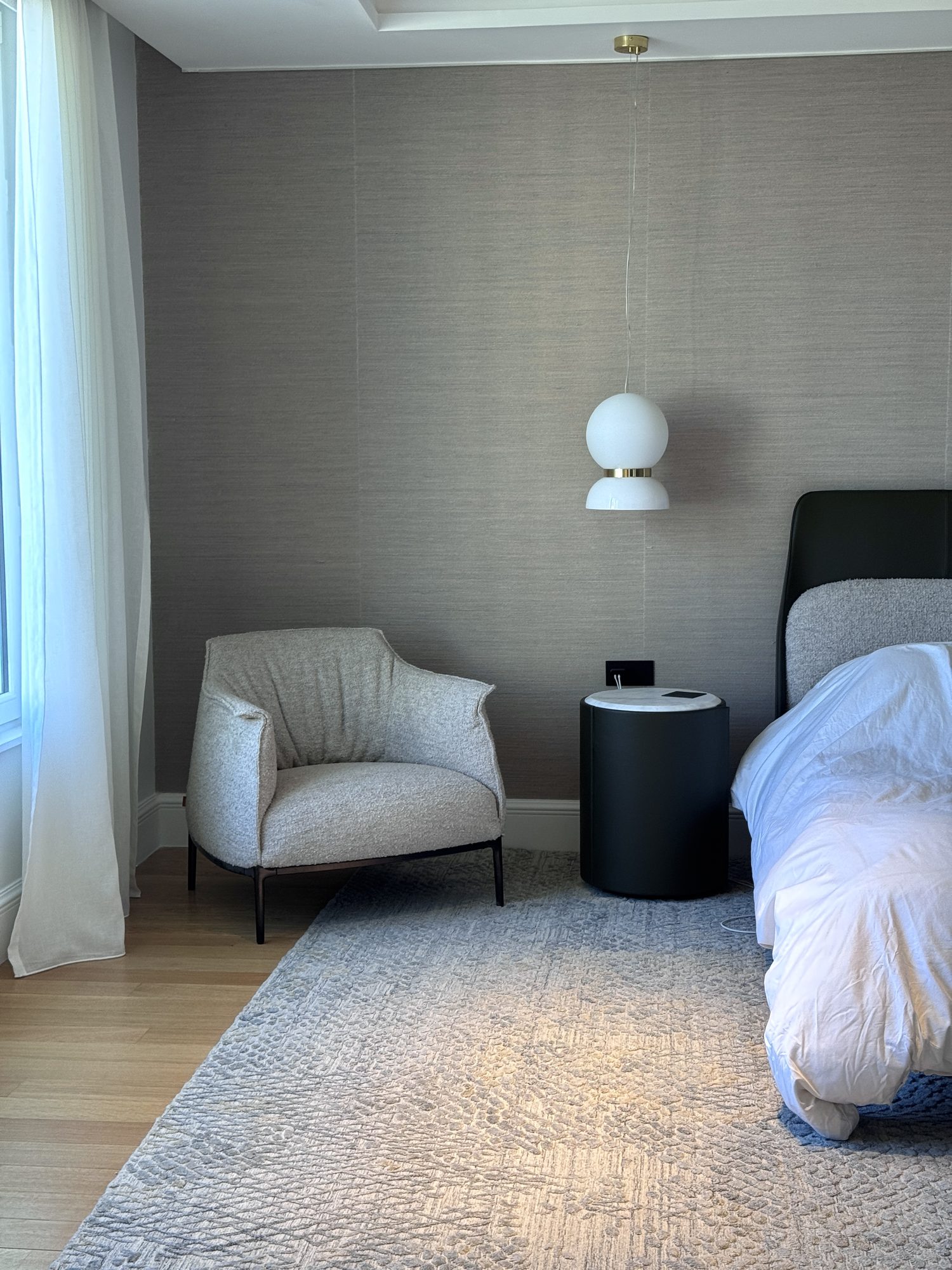Chambre aux murs texturés : fauteuil bouclé clair, suspension ronde en verre blanc et tête de lit noire