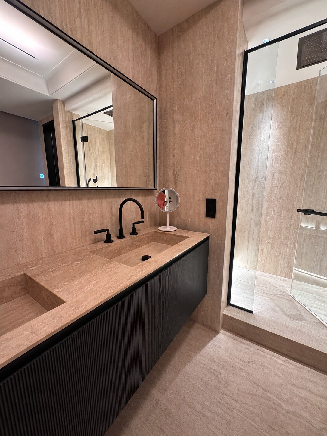 Salle de bains du duplex Maubourg en travertin, double vasque et meuble noir