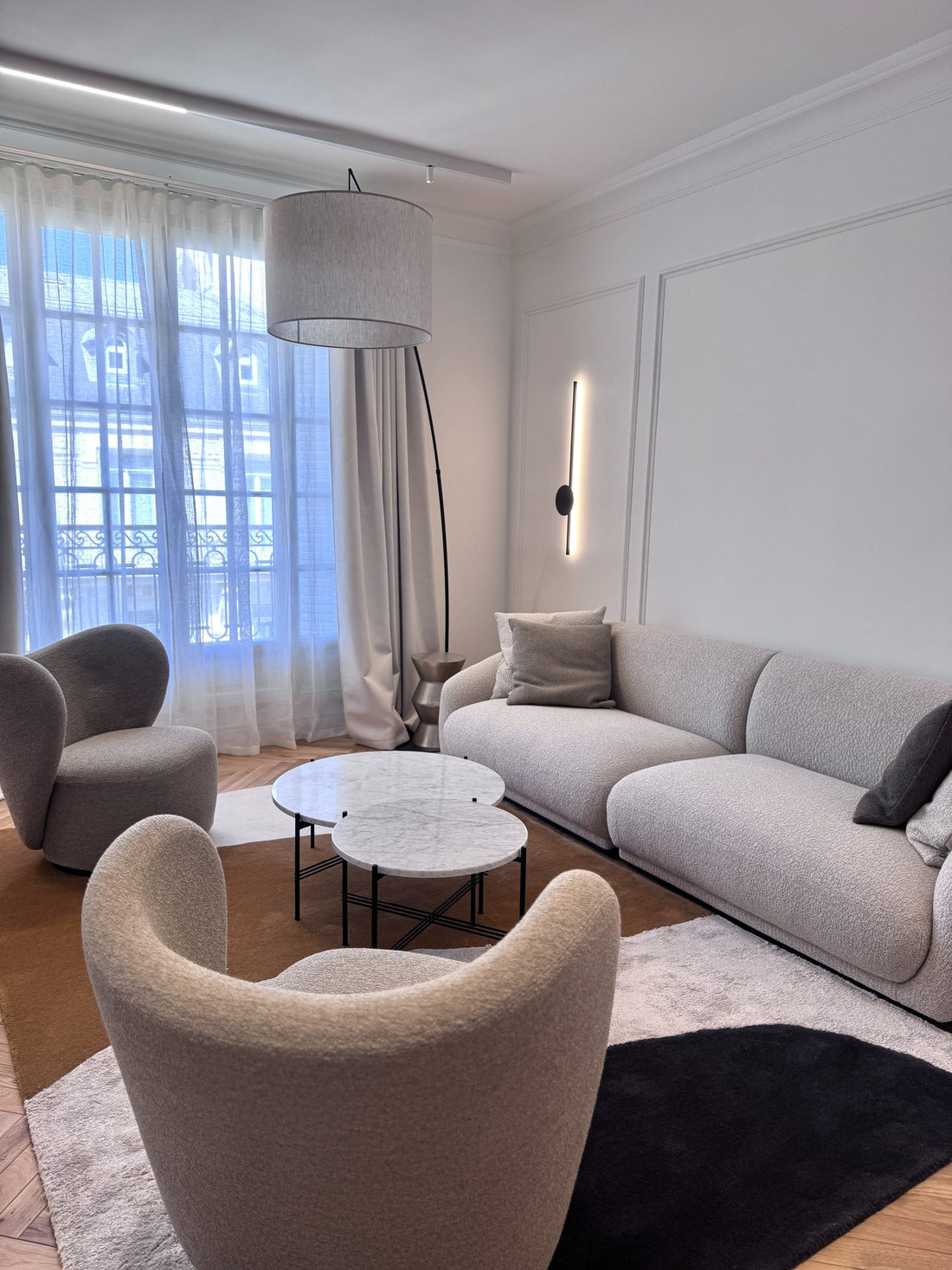 Salon du duplex Périer : canapé clair, fauteuils bouclés et fenêtres
