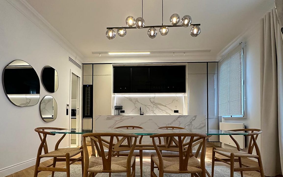Salle à manger du duplex Périer : table en verre, chaises en bois et cuisine en arrière-plan